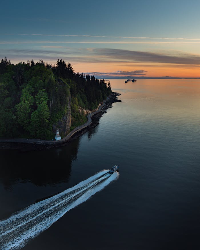 A motorboat speeds near Stanley Park, Vancouver, at sunset, surrounded by stunning coastal scenery.