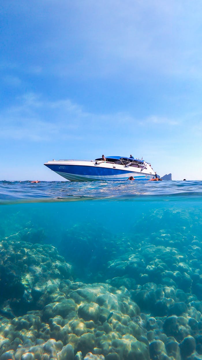 A speedboat floating above coral reefs in clear waters of Krabi, Thailand, under a bright blue sky.